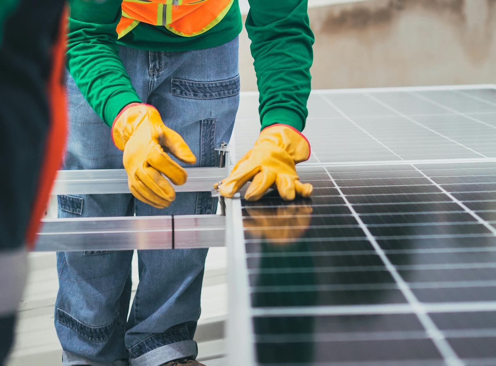 Worker in safety gear installing solar panels on a rooftop.